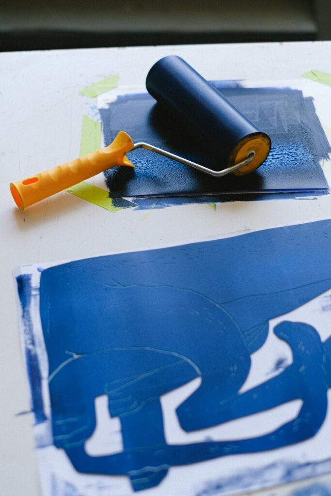 A paint roller with blue gouache creating a textured art piece on paper.