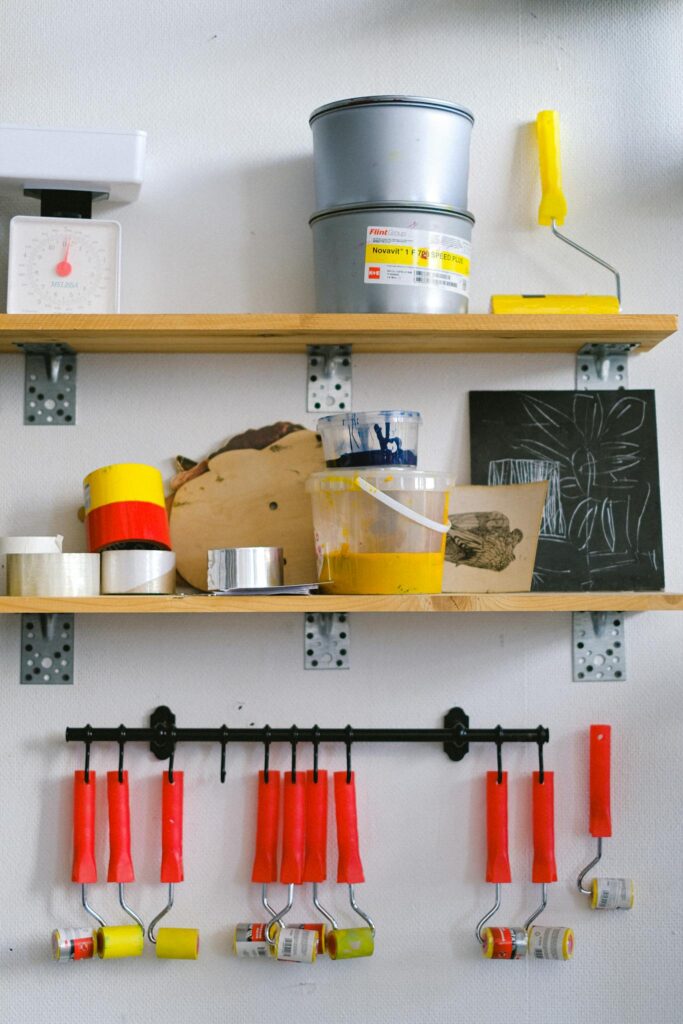 Shelves with paint colours in containers and paint rollers hanging on hooks on wall in art workshop